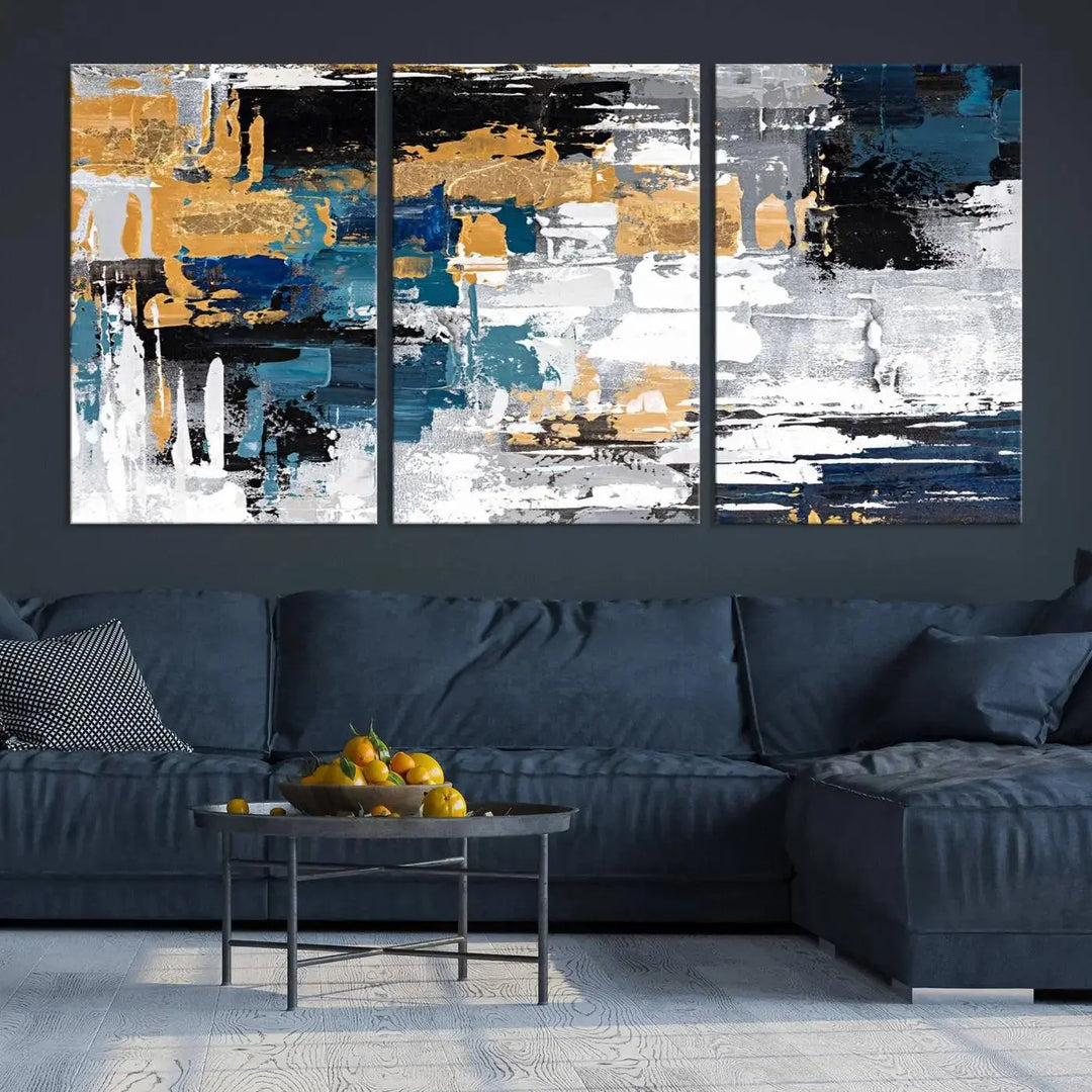 The Blue and Gold Abstract Canvas Wall Art – a triptych modern painting that's framed and ready to hang – features captivating brush strokes in blue, gold, black, and white to enhance the living room decor.