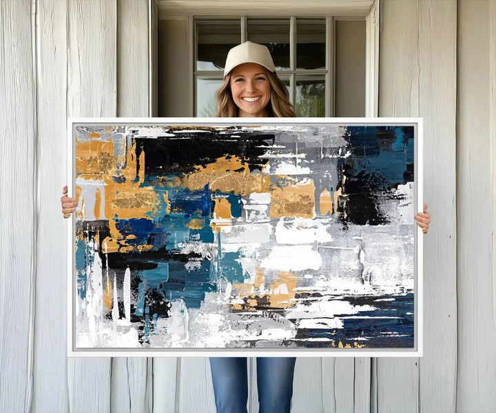 The Blue and Gold Abstract Canvas Wall Art – a triptych modern painting that's framed and ready to hang – features captivating brush strokes in blue, gold, black, and white to enhance the living room decor.