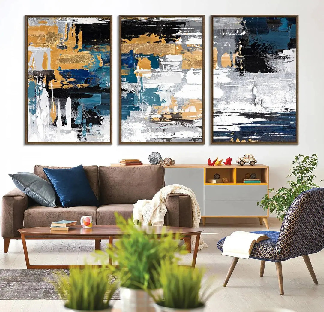 The Blue and Gold Abstract Canvas Wall Art – a triptych modern painting that's framed and ready to hang – features captivating brush strokes in blue, gold, black, and white to enhance the living room decor.