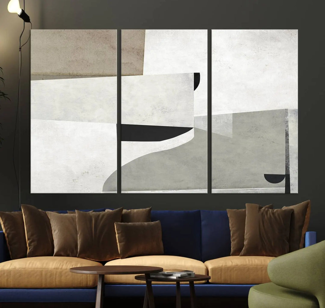 The Brown Gray Figures Abstract Wall Art Canvas Print is displayed as a triptych on a dark wall. The piece is gallery wrapped, offering a seamless finish and enhanced durability due to its UV-protective coating.