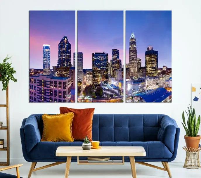 The Charlotte City Lights Sunset Purple Skyline Cityscape View Wall Art Canvas Print showcases a triptych of a city skyline with illuminated skyscrapers at dusk.