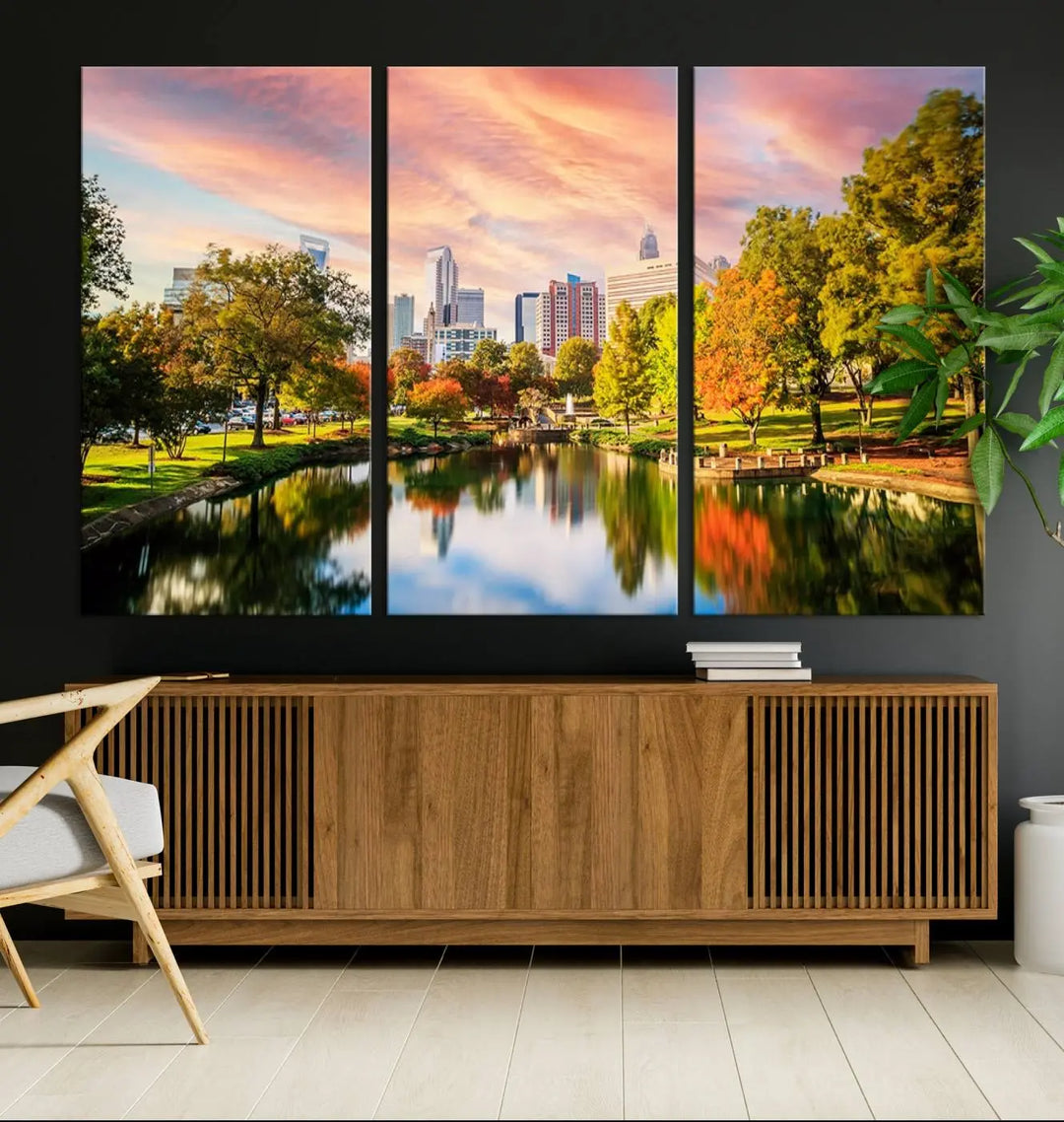 The "Charlotte City Park Sunset Pink and Orange Skyline Canvas Print" is elegantly displayed in a modern living room. Crafted on museum-quality canvas, this triptych wall art showcases a cityscape and park at sunset, complete with a UV-protective coating, and is ready to hang.