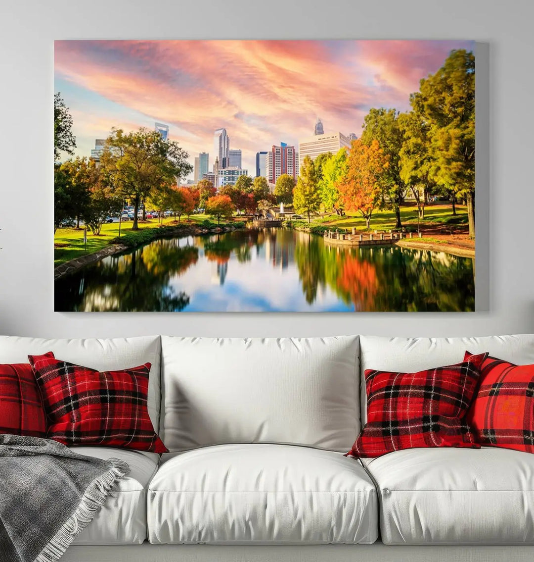 The "Charlotte City Park Sunset Pink and Orange Skyline Canvas Print" is elegantly displayed in a modern living room. Crafted on museum-quality canvas, this triptych wall art showcases a cityscape and park at sunset, complete with a UV-protective coating, and is ready to hang.