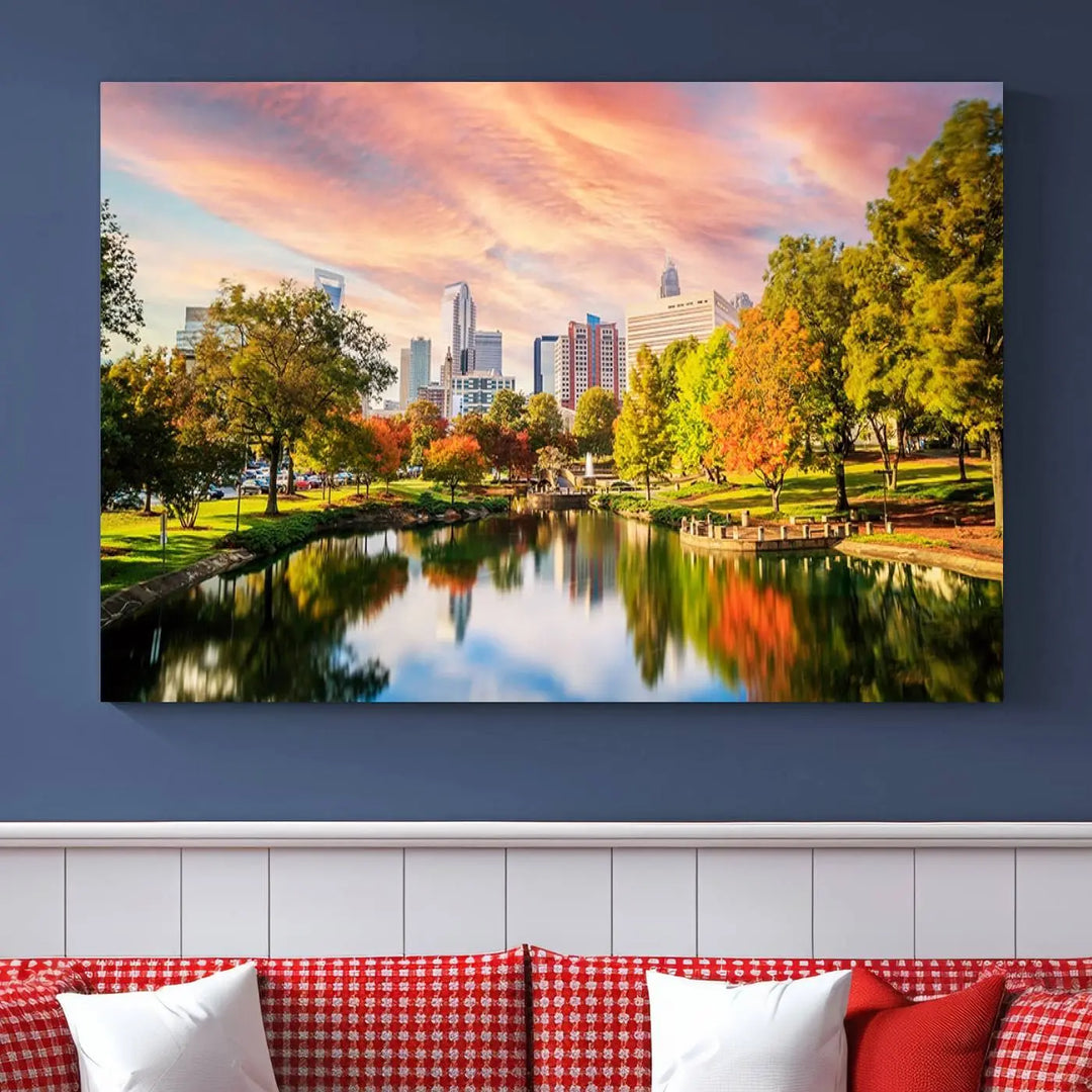 The "Charlotte City Park Sunset Pink and Orange Skyline Canvas Print" is elegantly displayed in a modern living room. Crafted on museum-quality canvas, this triptych wall art showcases a cityscape and park at sunset, complete with a UV-protective coating, and is ready to hang.