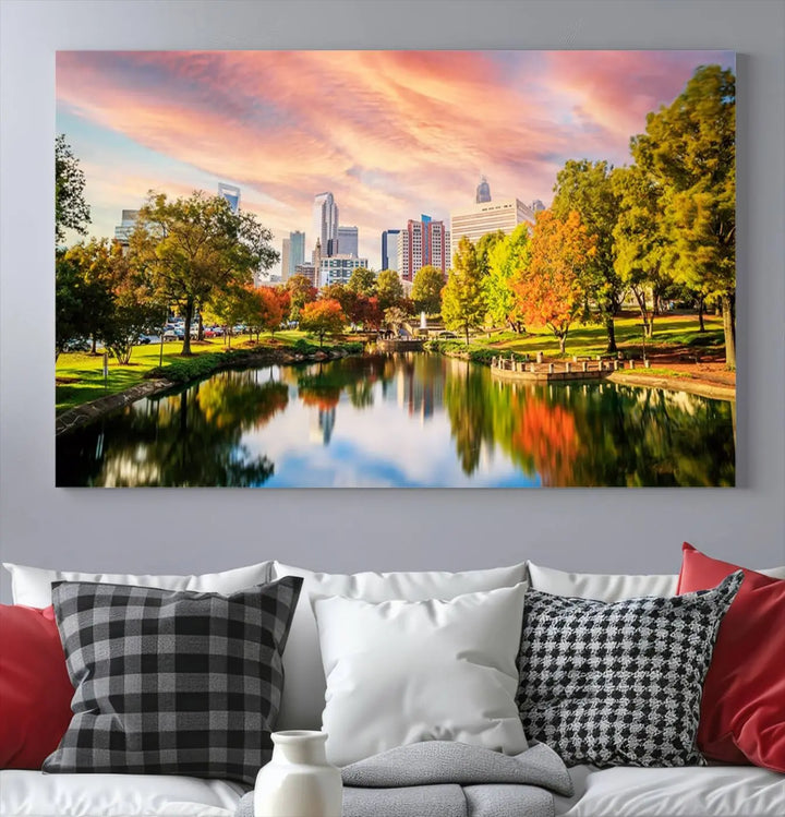 The "Charlotte City Park Sunset Pink and Orange Skyline Canvas Print" is elegantly displayed in a modern living room. Crafted on museum-quality canvas, this triptych wall art showcases a cityscape and park at sunset, complete with a UV-protective coating, and is ready to hang.