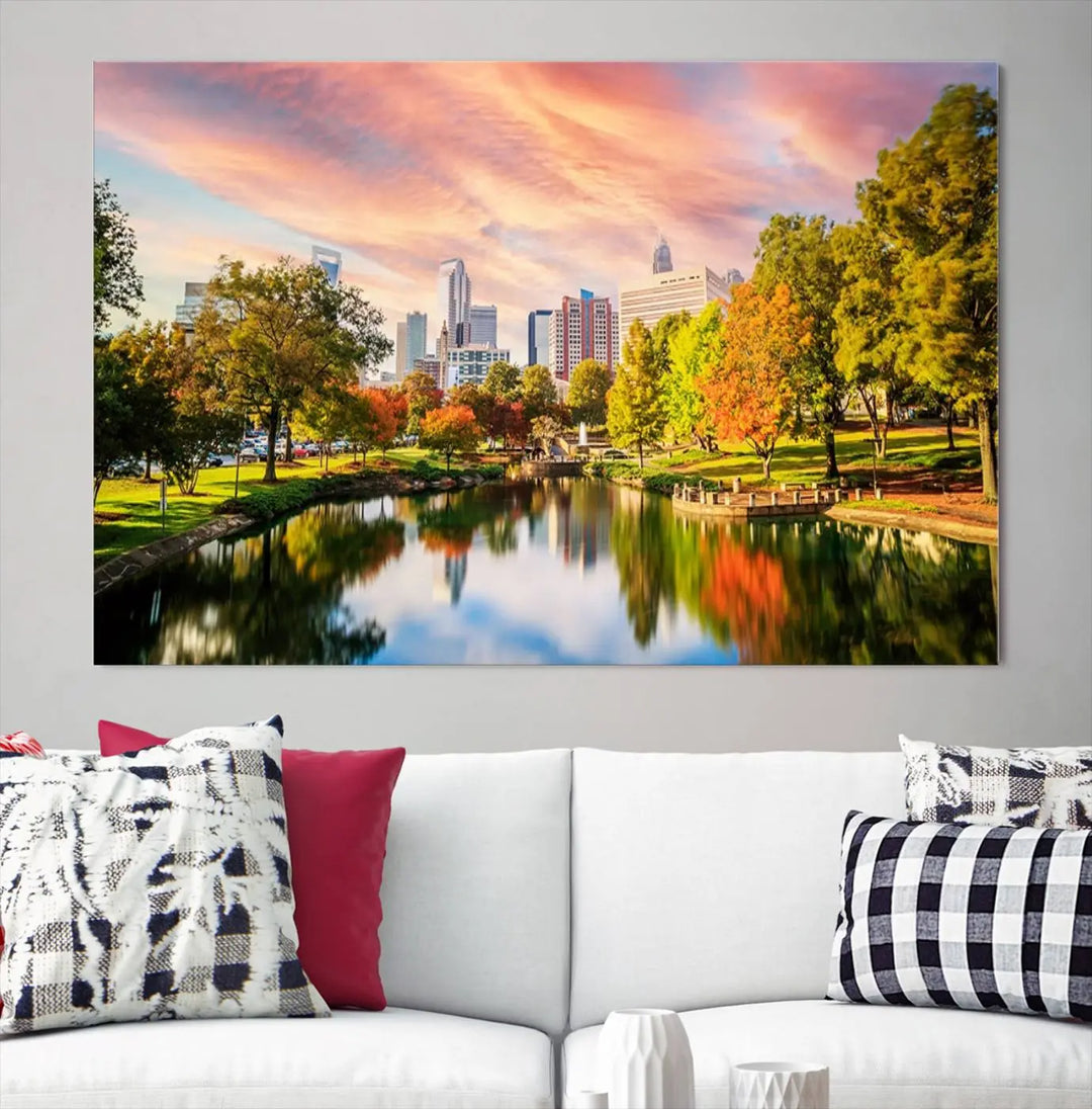 The "Charlotte City Park Sunset Pink and Orange Skyline Canvas Print" is elegantly displayed in a modern living room. Crafted on museum-quality canvas, this triptych wall art showcases a cityscape and park at sunset, complete with a UV-protective coating, and is ready to hang.