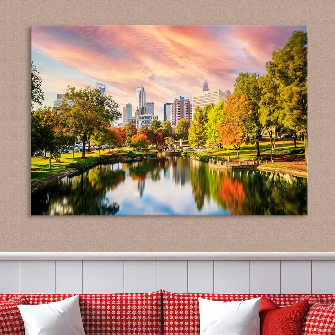 The "Charlotte City Park Sunset Pink and Orange Skyline Canvas Print" is elegantly displayed in a modern living room. Crafted on museum-quality canvas, this triptych wall art showcases a cityscape and park at sunset, complete with a UV-protective coating, and is ready to hang.