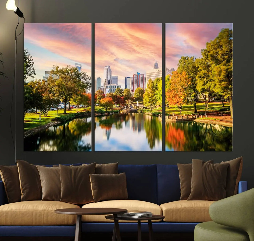 The "Charlotte City Park Sunset Pink and Orange Skyline Canvas Print" is elegantly displayed in a modern living room. Crafted on museum-quality canvas, this triptych wall art showcases a cityscape and park at sunset, complete with a UV-protective coating, and is ready to hang.