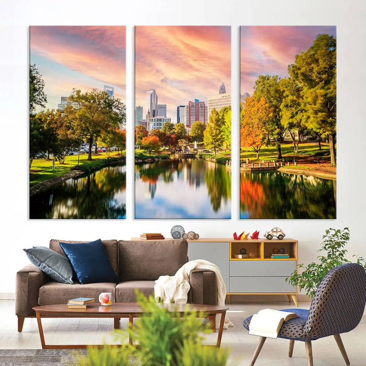 The "Charlotte City Park Sunset Pink and Orange Skyline Canvas Print" is elegantly displayed in a modern living room. Crafted on museum-quality canvas, this triptych wall art showcases a cityscape and park at sunset, complete with a UV-protective coating, and is ready to hang.