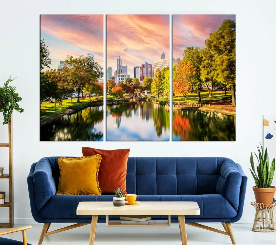 The "Charlotte City Park Sunset Pink and Orange Skyline Canvas Print" is elegantly displayed in a modern living room. Crafted on museum-quality canvas, this triptych wall art showcases a cityscape and park at sunset, complete with a UV-protective coating, and is ready to hang.