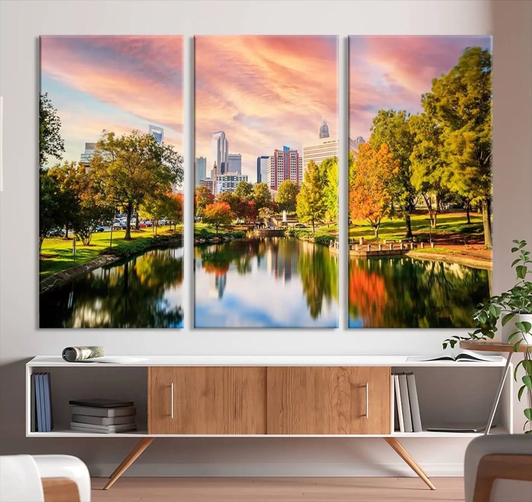 The "Charlotte City Park Sunset Pink and Orange Skyline Canvas Print" is elegantly displayed in a modern living room. Crafted on museum-quality canvas, this triptych wall art showcases a cityscape and park at sunset, complete with a UV-protective coating, and is ready to hang.