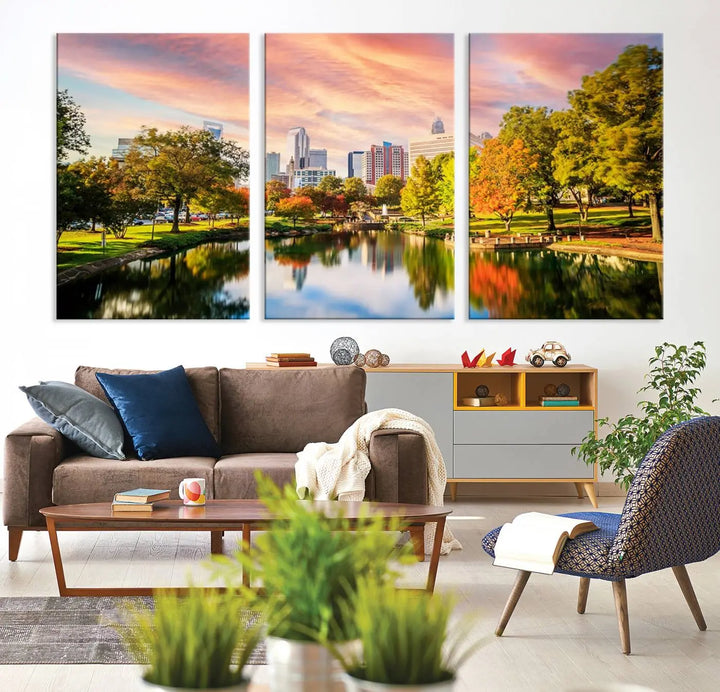 The "Charlotte City Park Sunset Pink and Orange Skyline Canvas Print" is elegantly displayed in a modern living room. Crafted on museum-quality canvas, this triptych wall art showcases a cityscape and park at sunset, complete with a UV-protective coating, and is ready to hang.