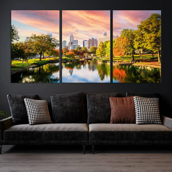 The "Charlotte City Park Sunset Pink and Orange Skyline Canvas Print" is elegantly displayed in a modern living room. Crafted on museum-quality canvas, this triptych wall art showcases a cityscape and park at sunset, complete with a UV-protective coating, and is ready to hang.