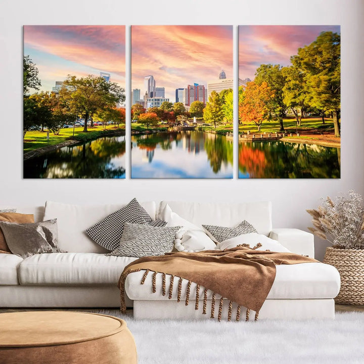 The "Charlotte City Park Sunset Pink and Orange Skyline Canvas Print" is elegantly displayed in a modern living room. Crafted on museum-quality canvas, this triptych wall art showcases a cityscape and park at sunset, complete with a UV-protective coating, and is ready to hang.