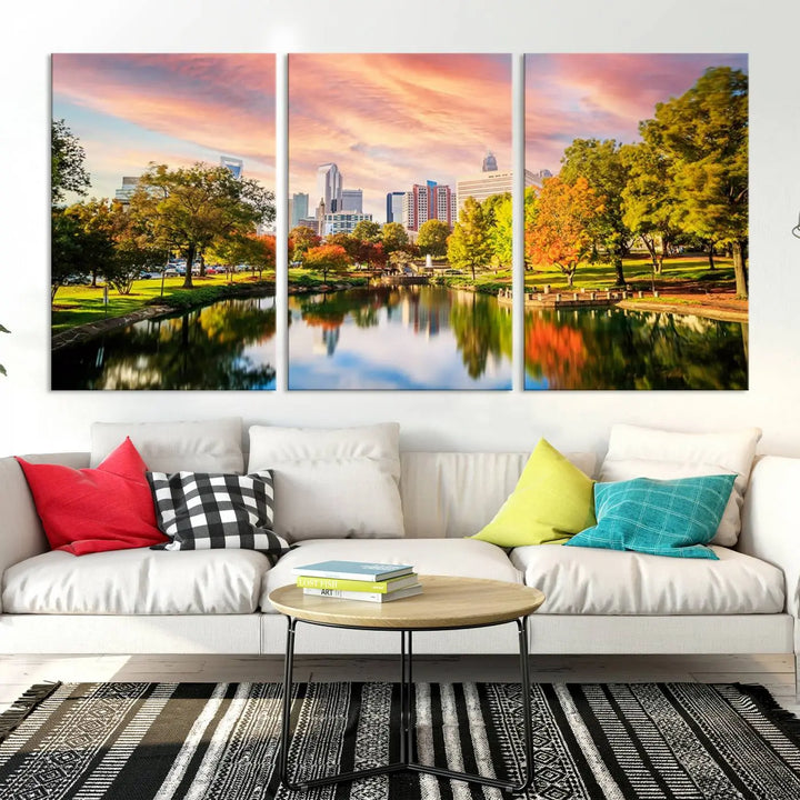 The "Charlotte City Park Sunset Pink and Orange Skyline Canvas Print" is elegantly displayed in a modern living room. Crafted on museum-quality canvas, this triptych wall art showcases a cityscape and park at sunset, complete with a UV-protective coating, and is ready to hang.