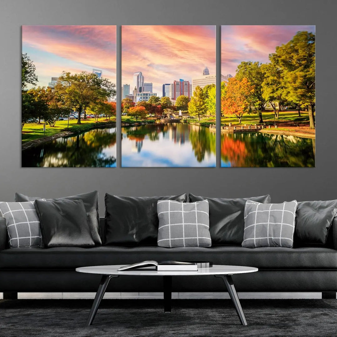 The "Charlotte City Park Sunset Pink and Orange Skyline Canvas Print" is elegantly displayed in a modern living room. Crafted on museum-quality canvas, this triptych wall art showcases a cityscape and park at sunset, complete with a UV-protective coating, and is ready to hang.