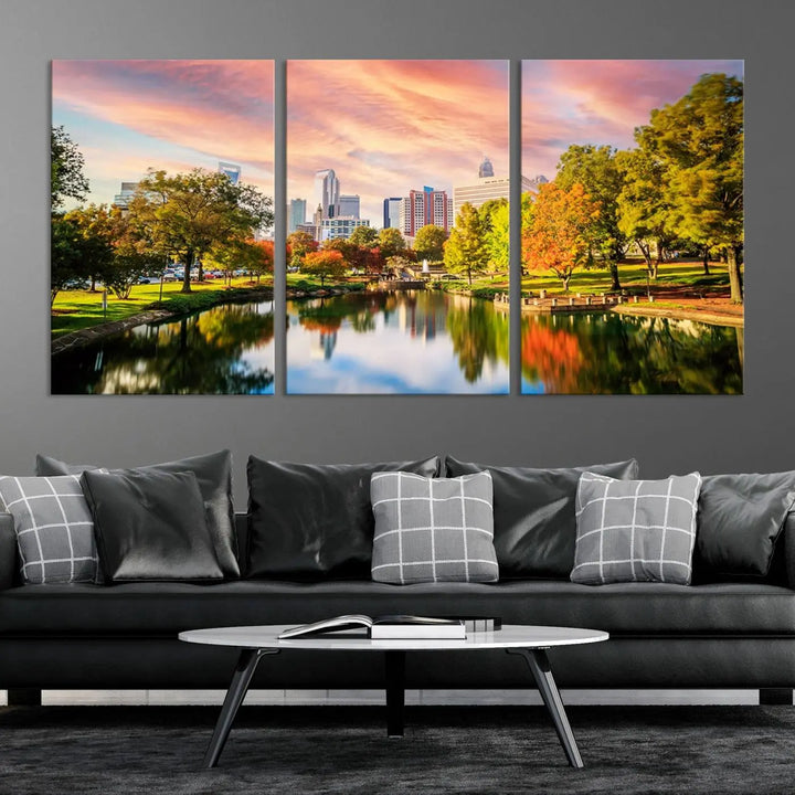 The "Charlotte City Park Sunset Pink and Orange Skyline Canvas Print" is elegantly displayed in a modern living room. Crafted on museum-quality canvas, this triptych wall art showcases a cityscape and park at sunset, complete with a UV-protective coating, and is ready to hang.