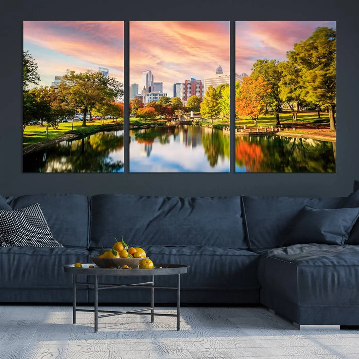 The "Charlotte City Park Sunset Pink and Orange Skyline Canvas Print" is elegantly displayed in a modern living room. Crafted on museum-quality canvas, this triptych wall art showcases a cityscape and park at sunset, complete with a UV-protective coating, and is ready to hang.