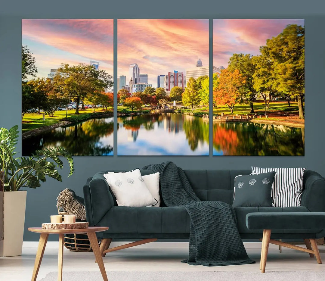 The "Charlotte City Park Sunset Pink and Orange Skyline Canvas Print" is elegantly displayed in a modern living room. Crafted on museum-quality canvas, this triptych wall art showcases a cityscape and park at sunset, complete with a UV-protective coating, and is ready to hang.