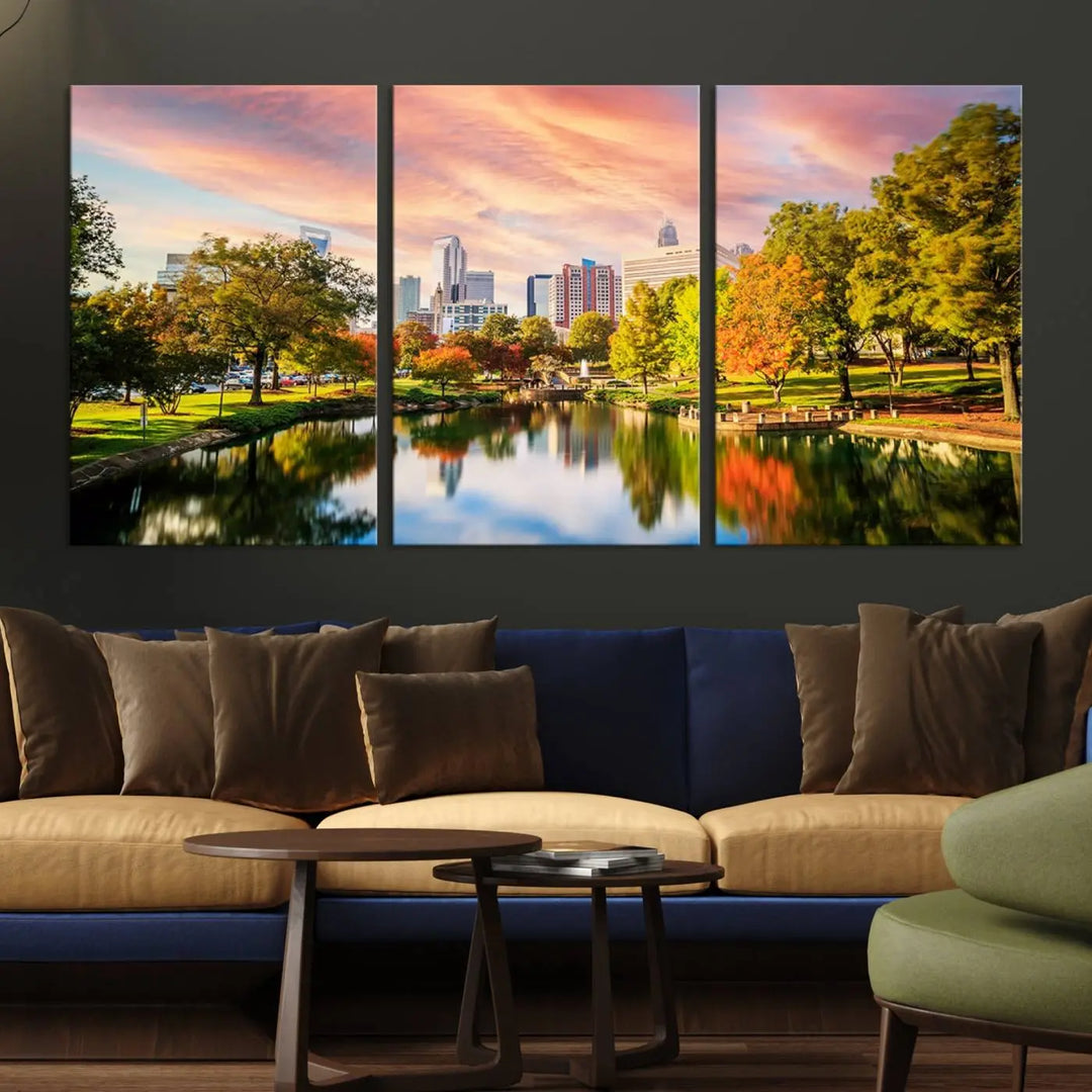 The "Charlotte City Park Sunset Pink and Orange Skyline Canvas Print" is elegantly displayed in a modern living room. Crafted on museum-quality canvas, this triptych wall art showcases a cityscape and park at sunset, complete with a UV-protective coating, and is ready to hang.