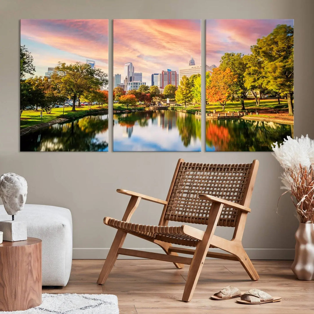 The "Charlotte City Park Sunset Pink and Orange Skyline Canvas Print" is elegantly displayed in a modern living room. Crafted on museum-quality canvas, this triptych wall art showcases a cityscape and park at sunset, complete with a UV-protective coating, and is ready to hang.