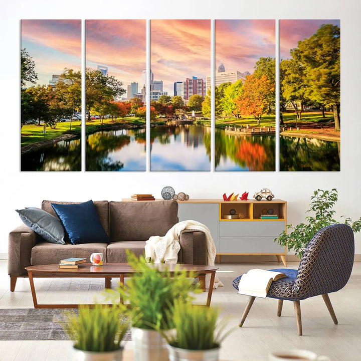 The "Charlotte City Park Sunset Pink and Orange Skyline Canvas Print" is elegantly displayed in a modern living room. Crafted on museum-quality canvas, this triptych wall art showcases a cityscape and park at sunset, complete with a UV-protective coating, and is ready to hang.