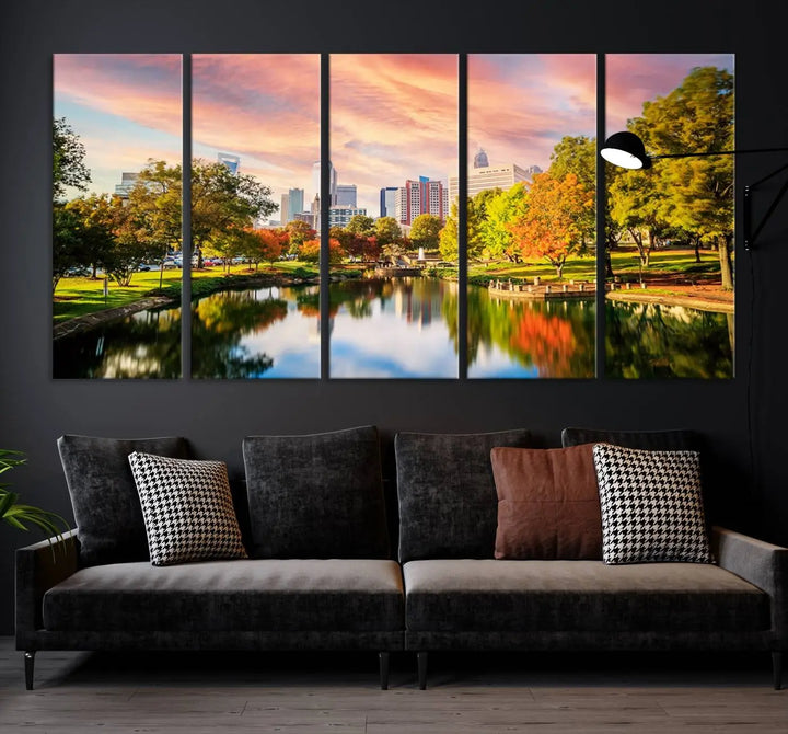 The "Charlotte City Park Sunset Pink and Orange Skyline Canvas Print" is elegantly displayed in a modern living room. Crafted on museum-quality canvas, this triptych wall art showcases a cityscape and park at sunset, complete with a UV-protective coating, and is ready to hang.