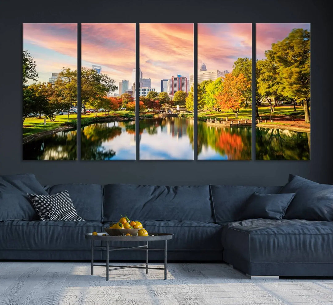 The "Charlotte City Park Sunset Pink and Orange Skyline Canvas Print" is elegantly displayed in a modern living room. Crafted on museum-quality canvas, this triptych wall art showcases a cityscape and park at sunset, complete with a UV-protective coating, and is ready to hang.