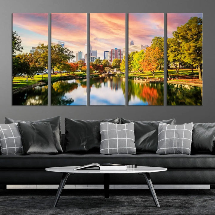 The "Charlotte City Park Sunset Pink and Orange Skyline Canvas Print" is elegantly displayed in a modern living room. Crafted on museum-quality canvas, this triptych wall art showcases a cityscape and park at sunset, complete with a UV-protective coating, and is ready to hang.