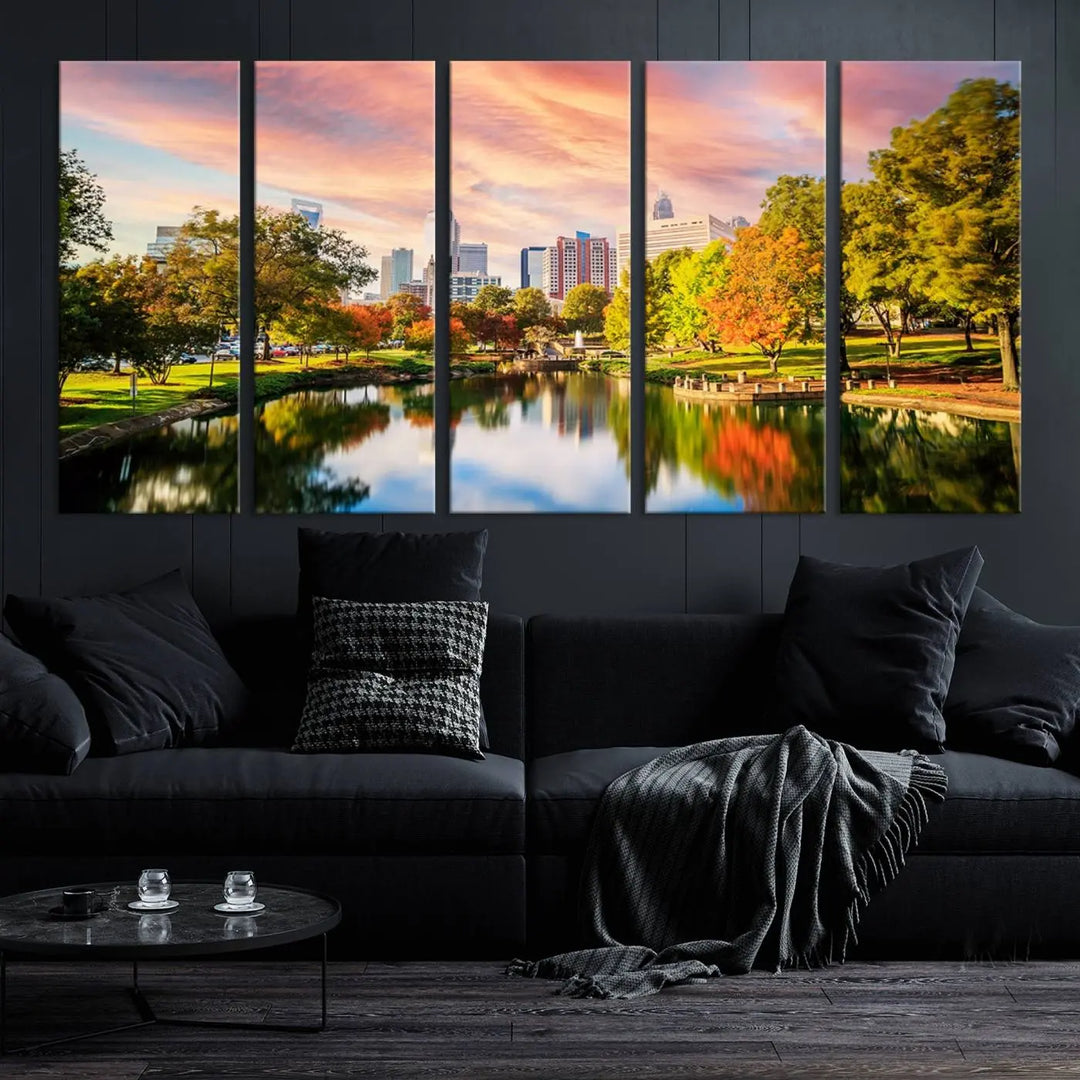 The "Charlotte City Park Sunset Pink and Orange Skyline Canvas Print" is elegantly displayed in a modern living room. Crafted on museum-quality canvas, this triptych wall art showcases a cityscape and park at sunset, complete with a UV-protective coating, and is ready to hang.