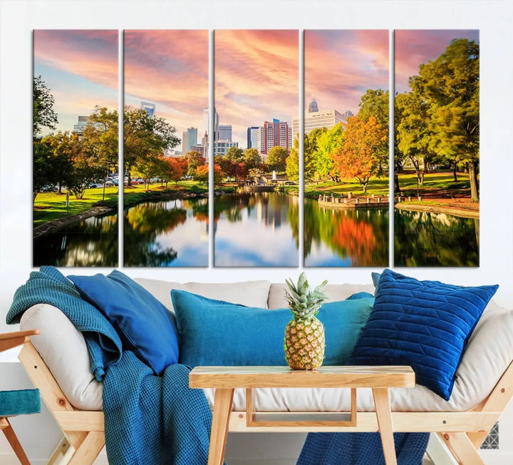 The "Charlotte City Park Sunset Pink and Orange Skyline Canvas Print" is elegantly displayed in a modern living room. Crafted on museum-quality canvas, this triptych wall art showcases a cityscape and park at sunset, complete with a UV-protective coating, and is ready to hang.