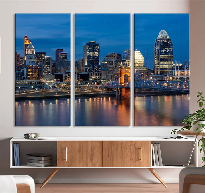 A triptych of the Cincinnati city lights night skyline, printed on museum-quality canvas with a UV-protective coating, hangs prominently on the wall.