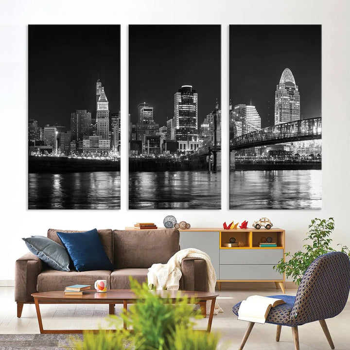 The Cincinnati City Lights Skyline Black and White Wall Art Cityscape Canvas Print elegantly adorns a modern living room. This museum-quality canvas triptych of a city skyline is enhanced by hand-assembled frames for added finesse, and you can enjoy free shipping on this stunning home addition.