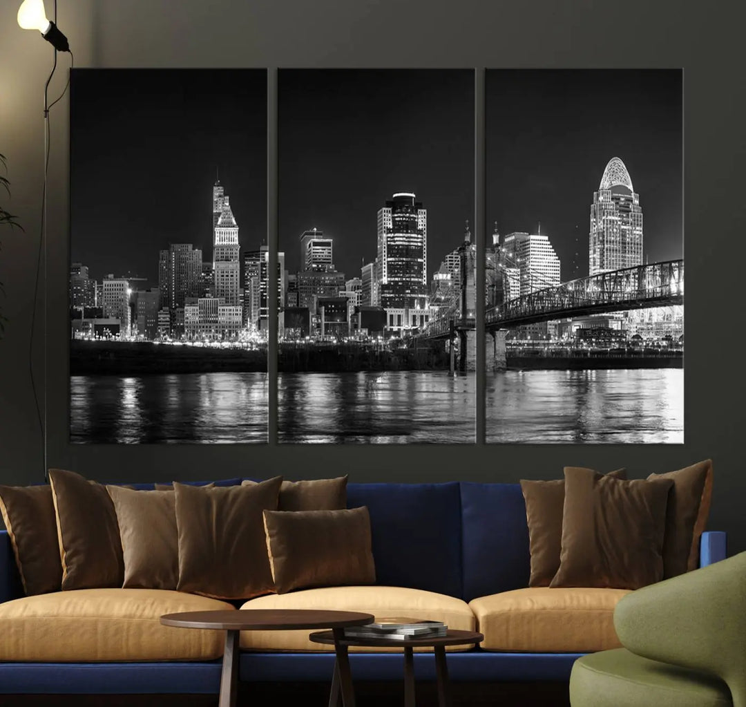 The Cincinnati City Lights Skyline Black and White Wall Art Cityscape Canvas Print elegantly adorns a modern living room. This museum-quality canvas triptych of a city skyline is enhanced by hand-assembled frames for added finesse, and you can enjoy free shipping on this stunning home addition.