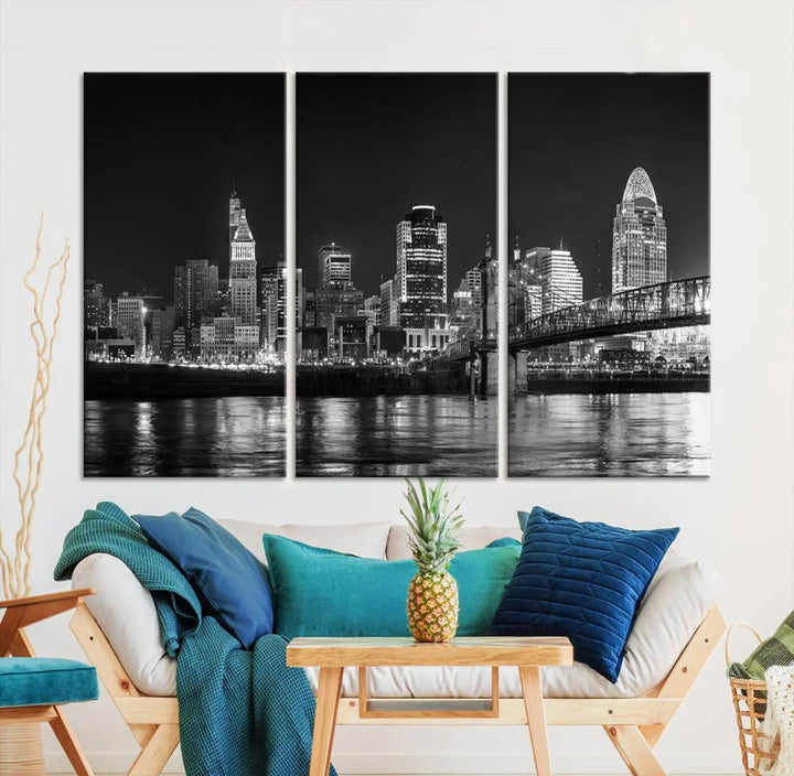 The Cincinnati City Lights Skyline Black and White Wall Art Cityscape Canvas Print elegantly adorns a modern living room. This museum-quality canvas triptych of a city skyline is enhanced by hand-assembled frames for added finesse, and you can enjoy free shipping on this stunning home addition.