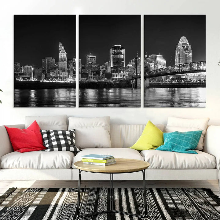 The Cincinnati City Lights Skyline Black and White Wall Art Cityscape Canvas Print elegantly adorns a modern living room. This museum-quality canvas triptych of a city skyline is enhanced by hand-assembled frames for added finesse, and you can enjoy free shipping on this stunning home addition.