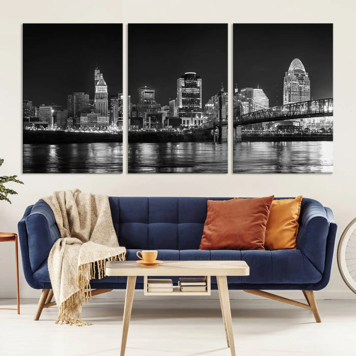 The Cincinnati City Lights Skyline Black and White Wall Art Cityscape Canvas Print elegantly adorns a modern living room. This museum-quality canvas triptych of a city skyline is enhanced by hand-assembled frames for added finesse, and you can enjoy free shipping on this stunning home addition.