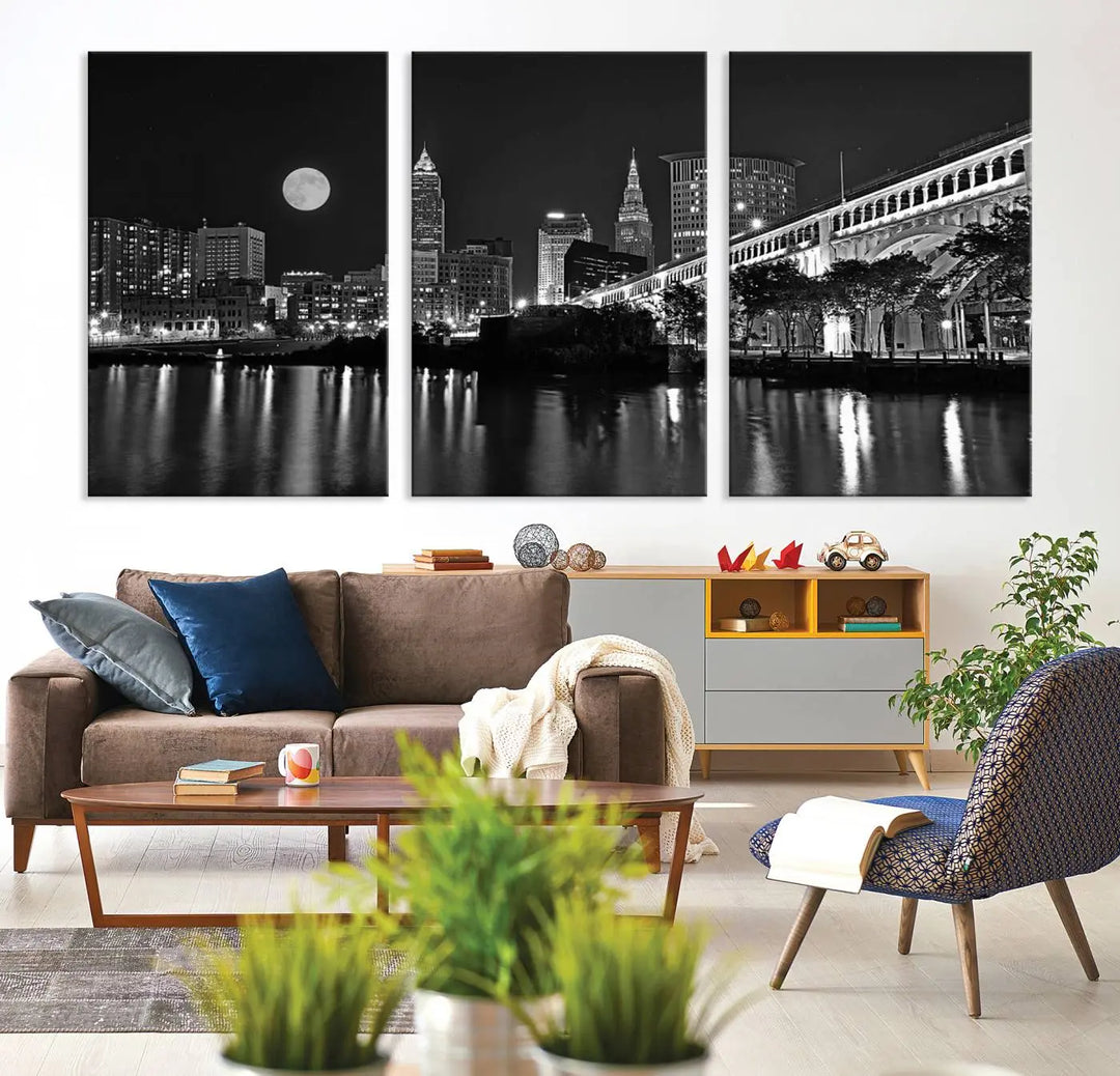 A modern living room features the "Cleveland Night Skyline Wall Art City Cityscape Canvas Print" on the wall, showcasing a moonlit skyline and river. It is professionally gallery wrapped on museum-quality canvas for enduring elegance.