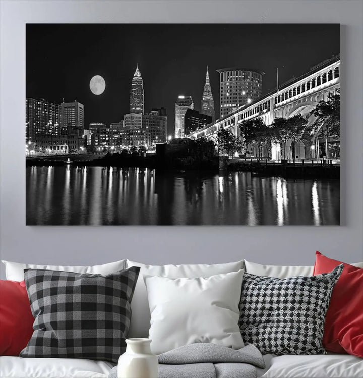 A modern living room features the "Cleveland Night Skyline Wall Art City Cityscape Canvas Print" on the wall, showcasing a moonlit skyline and river. It is professionally gallery wrapped on museum-quality canvas for enduring elegance.