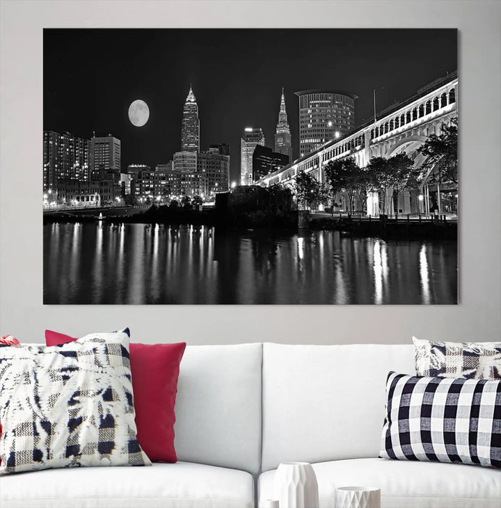 A modern living room features the "Cleveland Night Skyline Wall Art City Cityscape Canvas Print" on the wall, showcasing a moonlit skyline and river. It is professionally gallery wrapped on museum-quality canvas for enduring elegance.