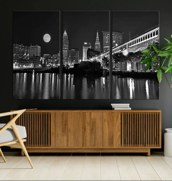 A modern living room features the "Cleveland Night Skyline Wall Art City Cityscape Canvas Print" on the wall, showcasing a moonlit skyline and river. It is professionally gallery wrapped on museum-quality canvas for enduring elegance.