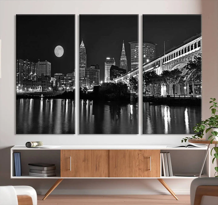 A modern living room features the "Cleveland Night Skyline Wall Art City Cityscape Canvas Print" on the wall, showcasing a moonlit skyline and river. It is professionally gallery wrapped on museum-quality canvas for enduring elegance.