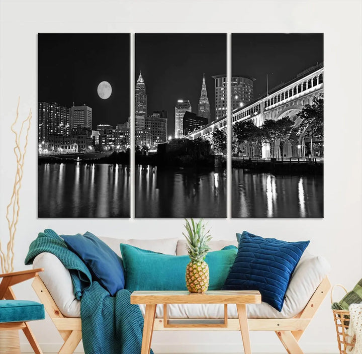 A modern living room features the "Cleveland Night Skyline Wall Art City Cityscape Canvas Print" on the wall, showcasing a moonlit skyline and river. It is professionally gallery wrapped on museum-quality canvas for enduring elegance.