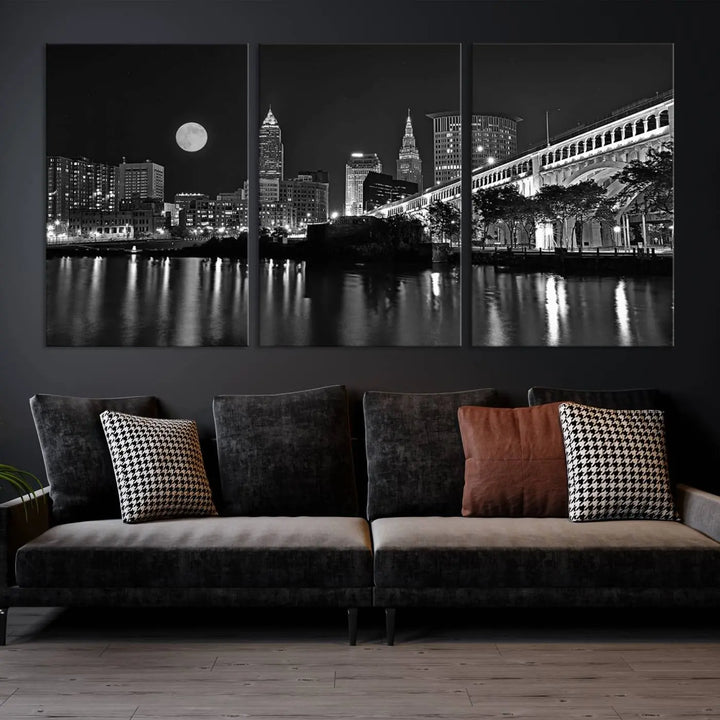 A modern living room features the "Cleveland Night Skyline Wall Art City Cityscape Canvas Print" on the wall, showcasing a moonlit skyline and river. It is professionally gallery wrapped on museum-quality canvas for enduring elegance.