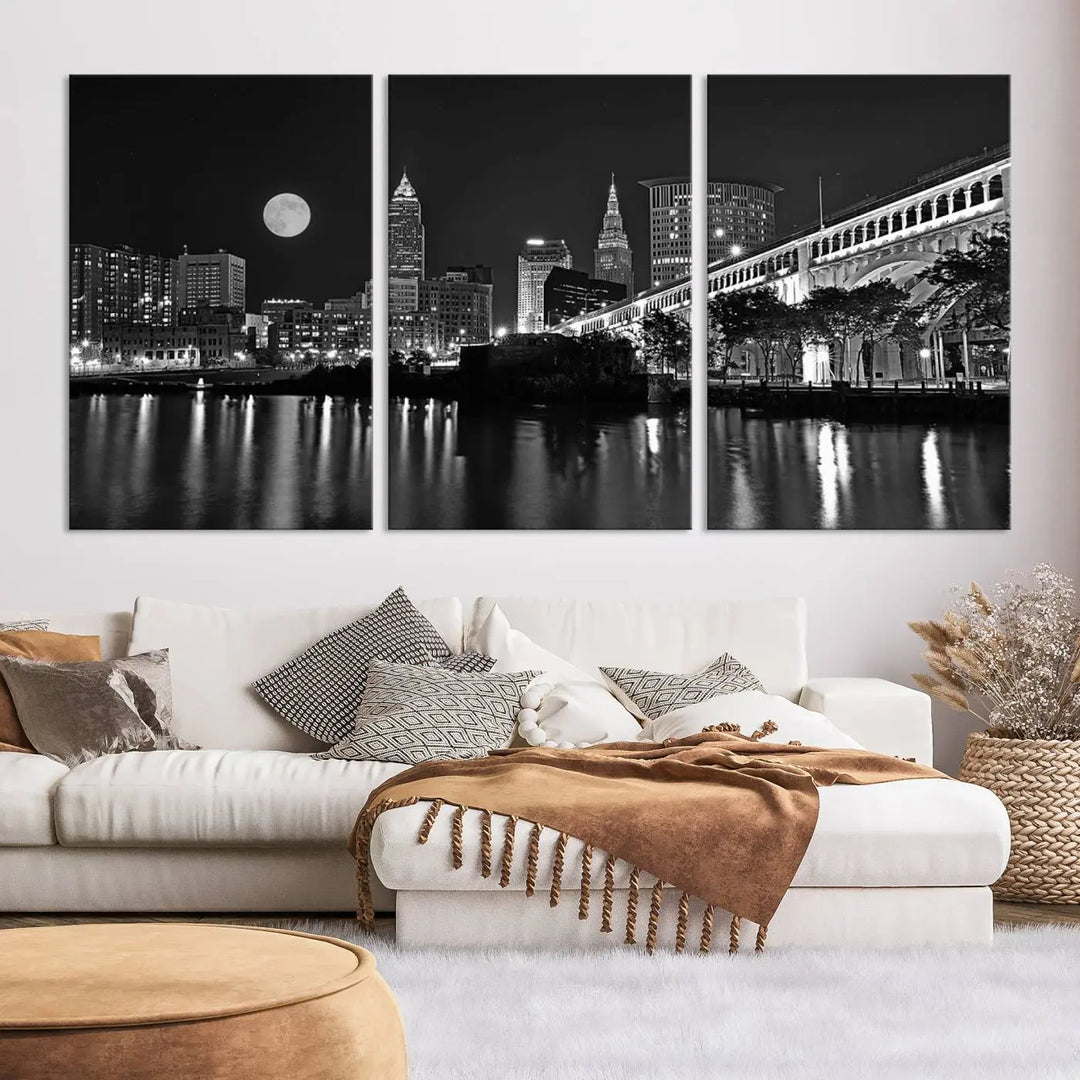 A modern living room features the "Cleveland Night Skyline Wall Art City Cityscape Canvas Print" on the wall, showcasing a moonlit skyline and river. It is professionally gallery wrapped on museum-quality canvas for enduring elegance.