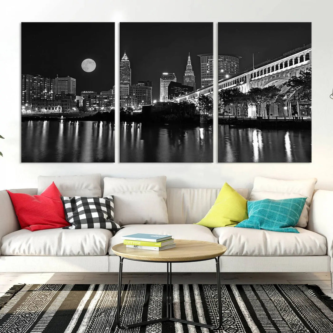 A modern living room features the "Cleveland Night Skyline Wall Art City Cityscape Canvas Print" on the wall, showcasing a moonlit skyline and river. It is professionally gallery wrapped on museum-quality canvas for enduring elegance.