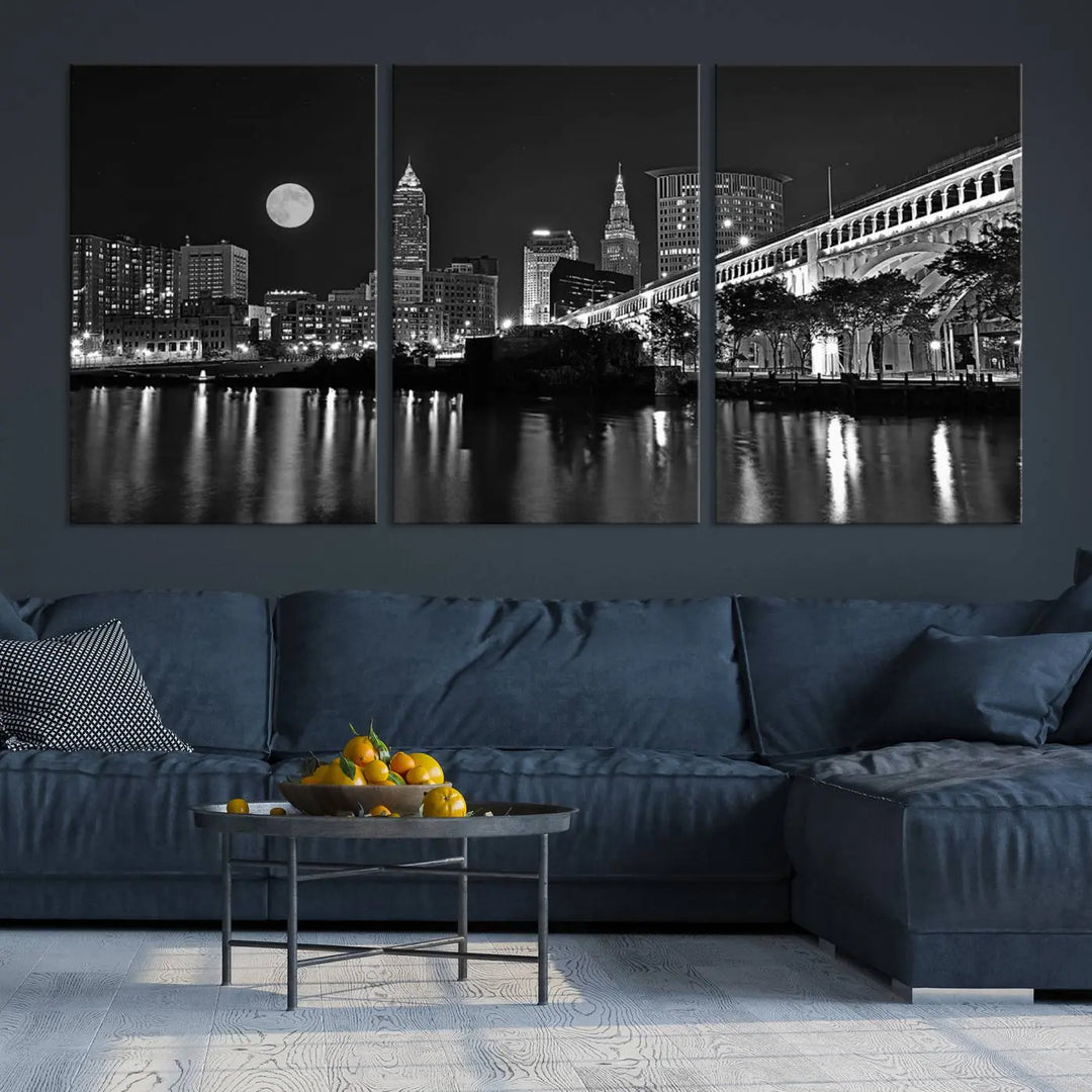 A modern living room features the "Cleveland Night Skyline Wall Art City Cityscape Canvas Print" on the wall, showcasing a moonlit skyline and river. It is professionally gallery wrapped on museum-quality canvas for enduring elegance.