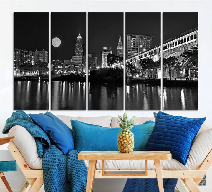 A modern living room features the "Cleveland Night Skyline Wall Art City Cityscape Canvas Print" on the wall, showcasing a moonlit skyline and river. It is professionally gallery wrapped on museum-quality canvas for enduring elegance.