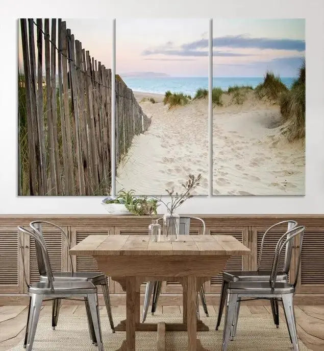 The Coastal Beach Fence Wall Art Ocean Landscape Canvas Print, featuring a triptych of a sandy beach scene with dunes and fences, is gallery wrapped on museum-quality canvas and displayed on a modern dark wall.