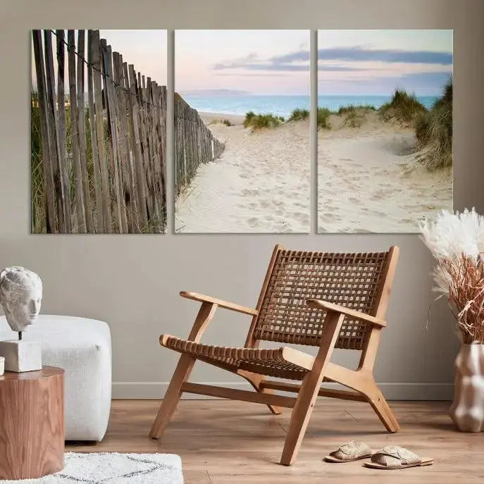 The Coastal Beach Fence Wall Art Ocean Landscape Canvas Print, featuring a triptych of a sandy beach scene with dunes and fences, is gallery wrapped on museum-quality canvas and displayed on a modern dark wall.